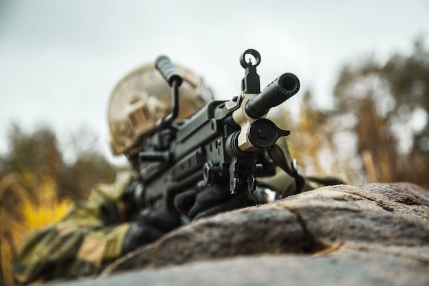 노르웨이 속력 특수부대 FSK 병사가 숲에서 사격을 가하고 있다. 야전 위장복, 전투 헬멧 및 안경 착용