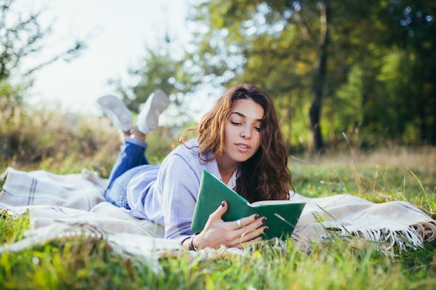 Nostalgic teenage girl is sitting in the park and reading book