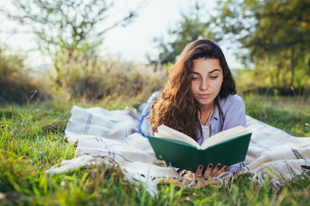 Nostalgic teenage girl is sitting in the park and reading book