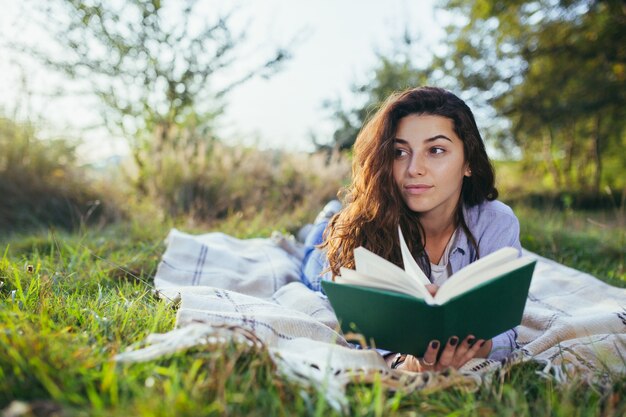 Nostalgic teenage girl is sitting in the park and reading book