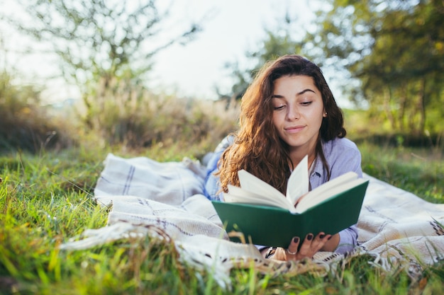 Nostalgic teenage girl is sitting in the park and reading book