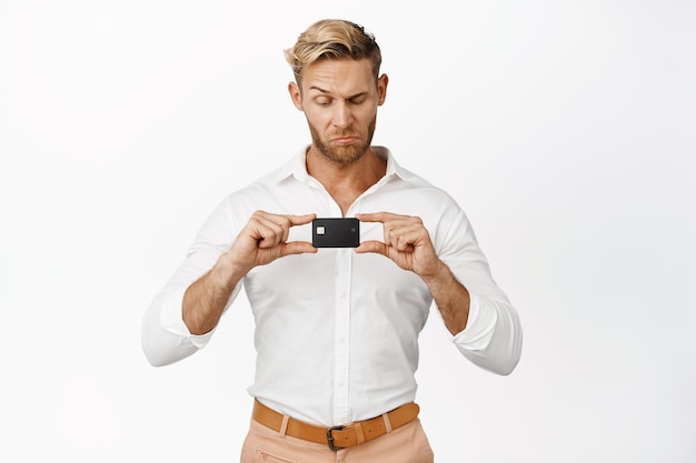Фото Неплохо впечатленный бизнесмен одобрительно кивает и смотрит на кредитную карту, стоящую на белом фоне