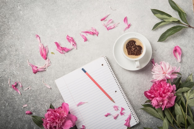 Note book, peonies and cup of coffee on light concrete backgrounds with text June