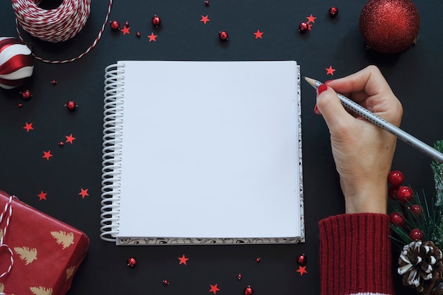 Note pad on black festive background with red decoration. Christmas concept