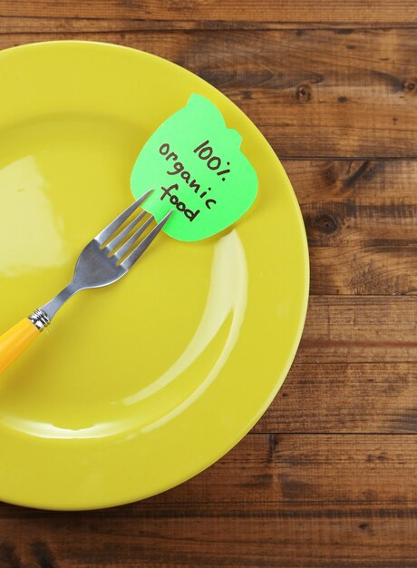 Note paper with message attached to fork on plate on color wooden background