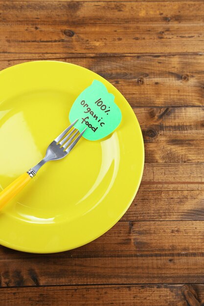 Note paper with message attached to fork on plate on color wooden background