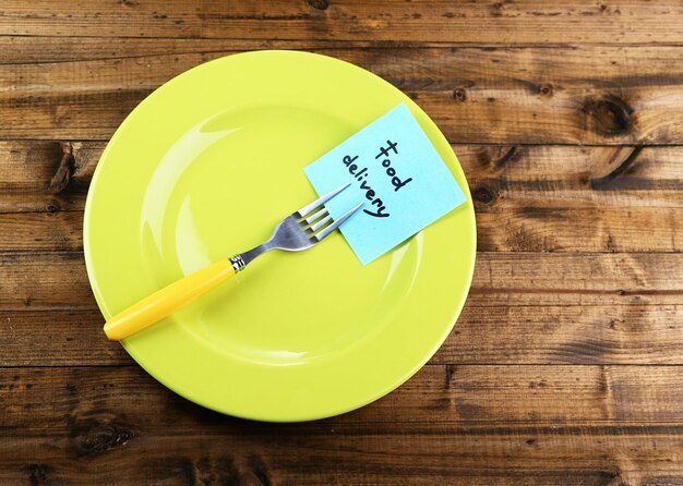 Photo note paper with message attached to fork on plate on color wooden background