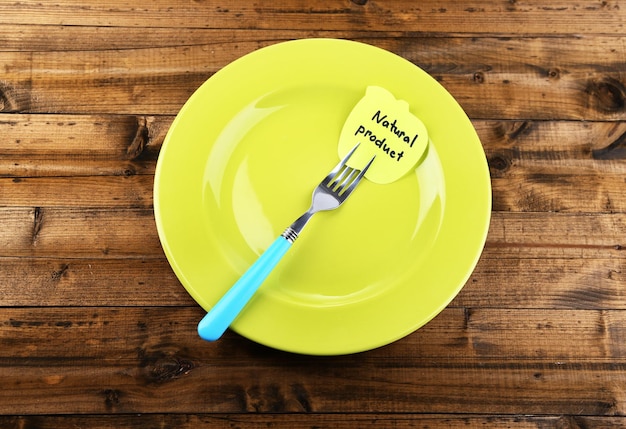 Note paper with message attached to fork on plate on color wooden background