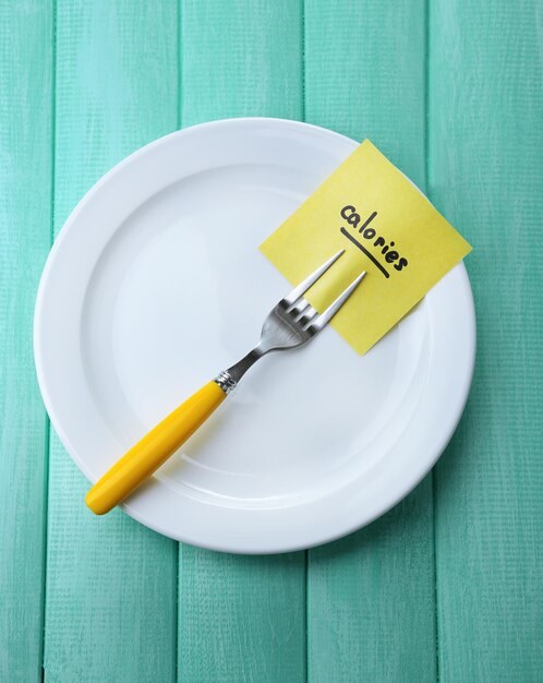 Note paper with message attached to fork on plate on wooden background