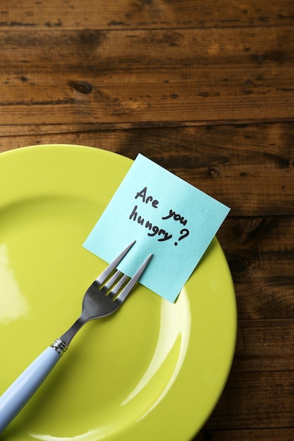 Note paper with message attached to fork on plate on wooden background