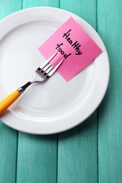 Note paper with message attached to fork on plate on wooden background