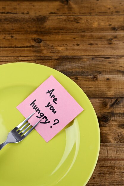 Photo note paper with message attached to fork on plate on wooden background