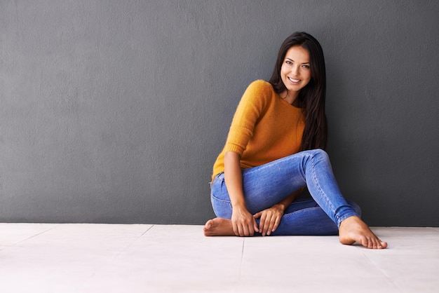 Note to self Ontspan Portret van een aantrekkelijke jonge vrouw die tegen een grijze muur zit