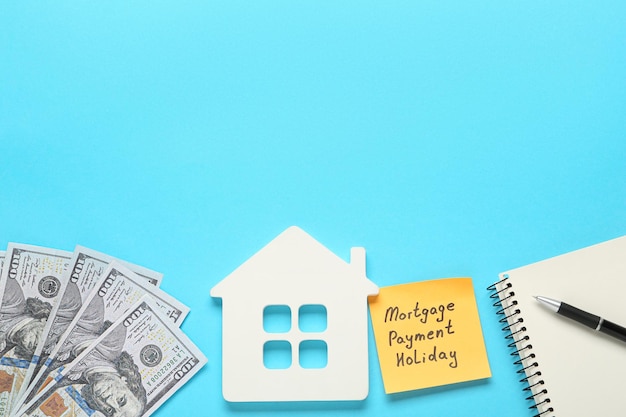 Photo note with words mortgage payment holiday house model notebook and money on light blue background flat lay space for text