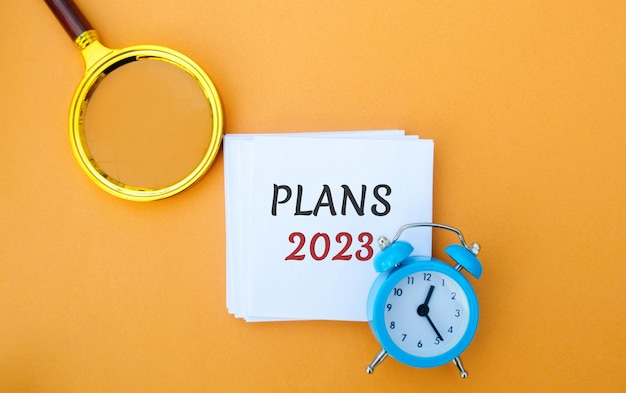 Note with words Plans 2023 Setting goals and planning targets for the next year Motivation vision Business and finance concept Magnifying glass and alarm clock