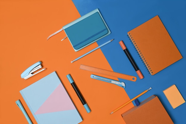 Фото Ноутбук и канцелярские товары на двухцветном синем и оранжевом фоне.
