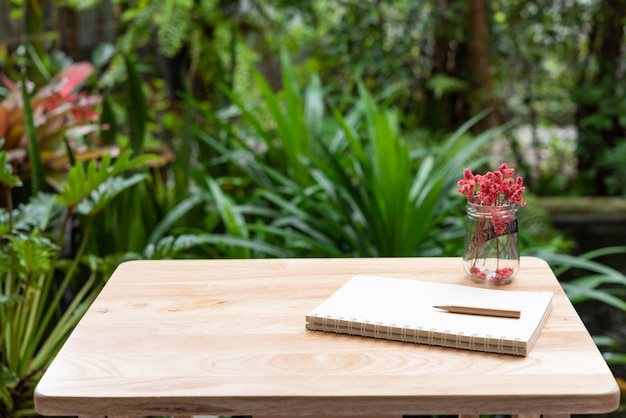 Notebook, bruin potlood en mooie rode gedroogde bloem in glazen vaas op houten tafel