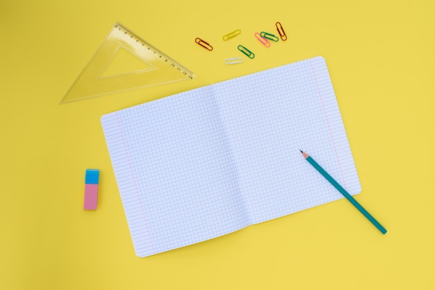 Notebook in a cage with a pencil, eraser, ruler, paper clips on a yellow background. Concept back to school. Place for text.