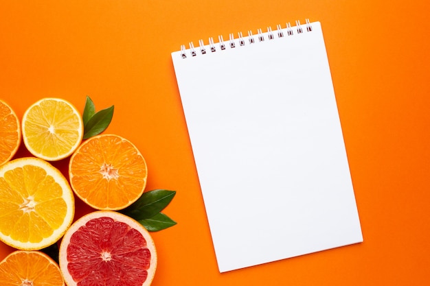 オレンジ色の背景上のノートと柑橘系の果物