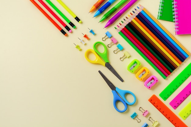 Notebook, colored pencils, ruler, pen, eraser, sharpener and school and office stationery on yellow background.