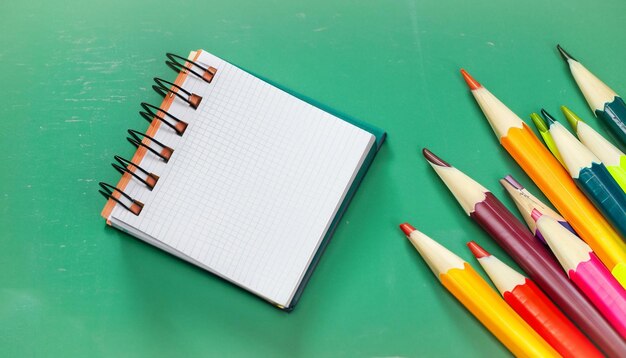 Notebook and colorful pencils on a Table closeup green board background generative ai