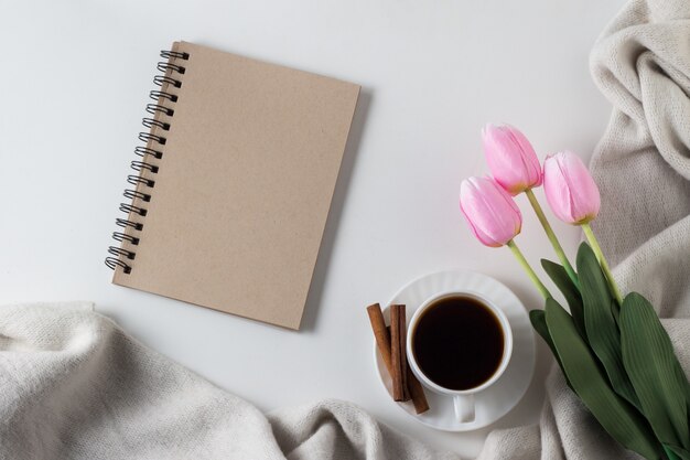 Notebook, cup of hot coffee, scarf, tulips on white surface. Spring Concept. Flat lay, top view