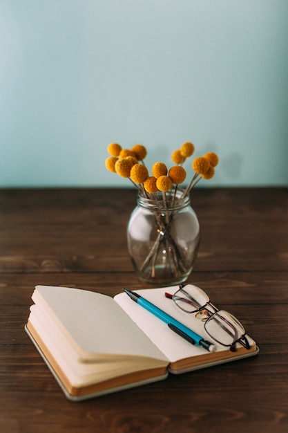 Notebook, flowers, pen and glasses.