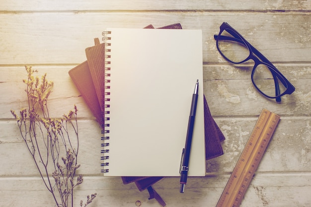 Notebook and glasses on grunge wooden background with vintage filter