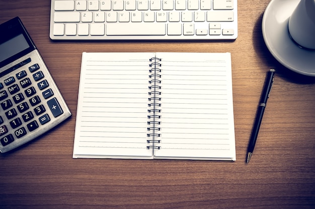 Notebook is on the table with calculator and coffee and computer keyboard. 