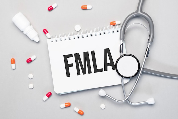 In the notebook is the text FMLA, next to a stethoscope, pills and glasses.