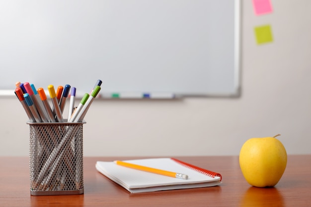 Notebook, kleurpotloden en een appel op tafel in de klas