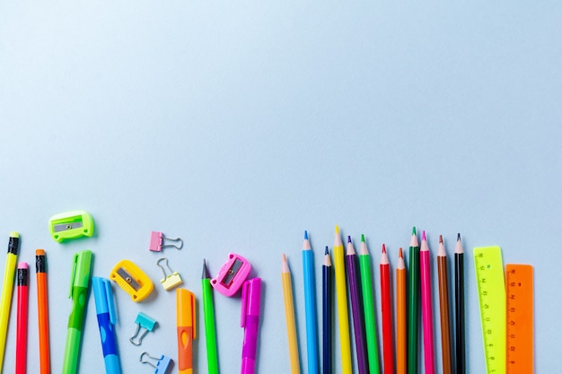 Notebook, kleurpotloden, liniaal, pen, gum, puntenslijper en school en kantoorbenodigdheden op blauwe achtergrond.