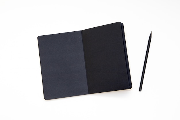 Notebook met zwart papier en potlood op witte achtergrond.