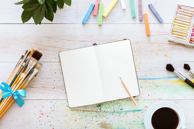 Notebook mock up with art supplies on white wooden table, top view, copy space