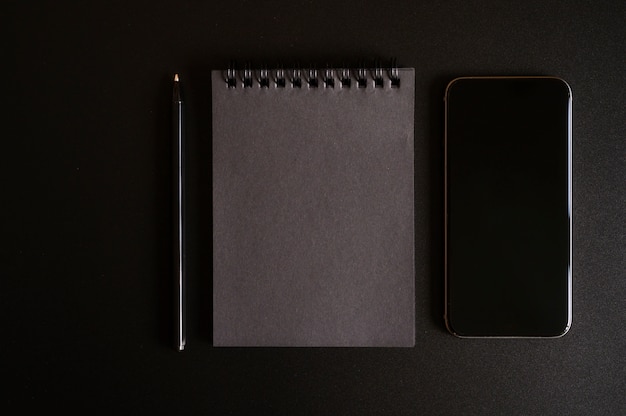 Foto notebook op een veer met zwarte lakens, en een pen, en mobiele telefoon op zwart