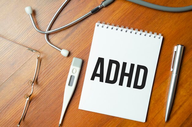 Notebook page with text ADHD Attention Deficit Hyperactivity Disorder on a table with a stethoscope and pen medical concept