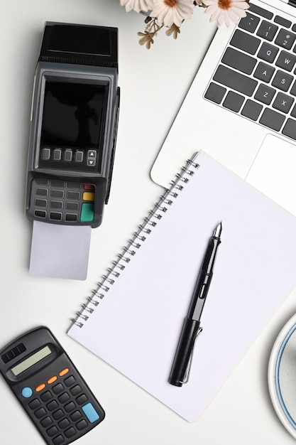 Notebook, payment terminal, laptop computer and calculator on white desk.