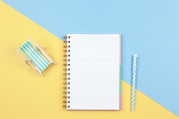 Notebook, pen, deck chair on two-color background yellow and blue, copy space, flat lay.