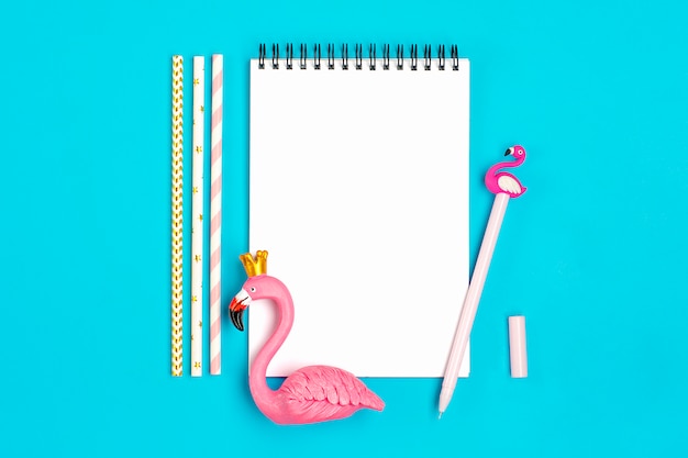 Notebook, pen, flamingo figure, smartphone, drinking paper straws on blue background