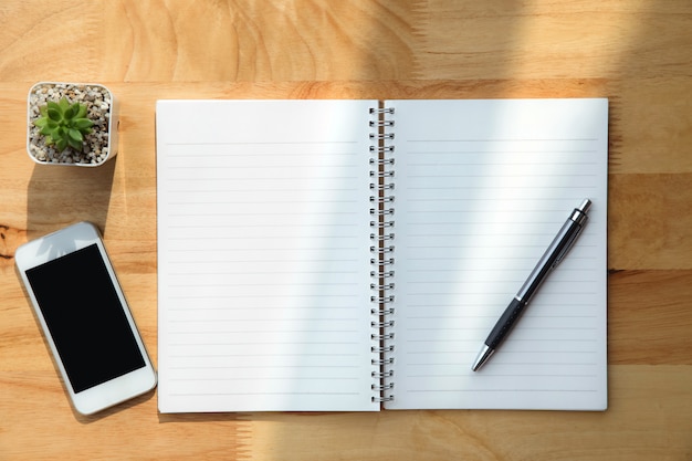 Notebook ,pen ,green plant and smartphone on wooden background