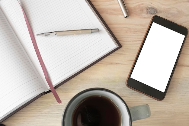 Notebook pen kopje thee en mobiele telefoon met wit scherm voor reclame op houten achtergrond