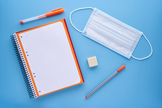 Notebook and pen with a mask on a blue background. Back to school concept and protection against covid.