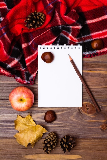 Photo notebook, pencil, blanket and gifts of autumn on a wooden background.