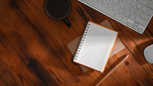 Notebook pencil coffee cup and wireless keyboard on wooden background Top view