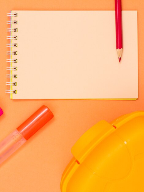 Notebook, pencil, red felt-tip pen and yellow lunch box on pink background.