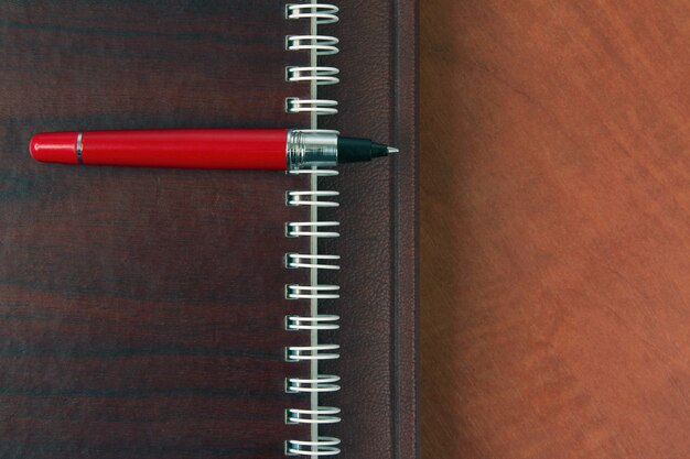 The notebook and a red pen lying on wooden desk