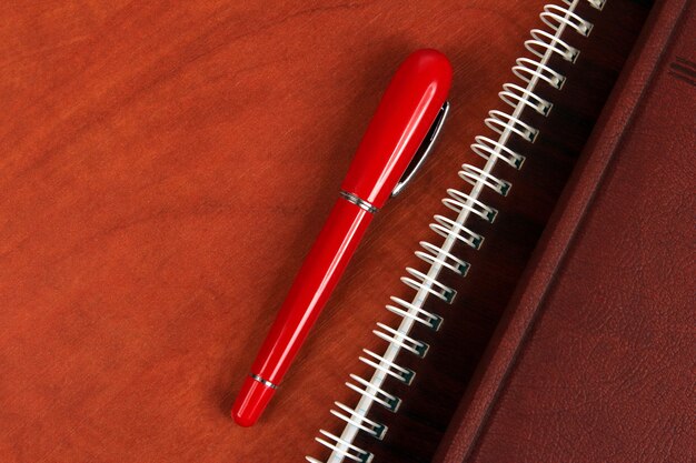 The notebook and a red pen lying on wooden desk