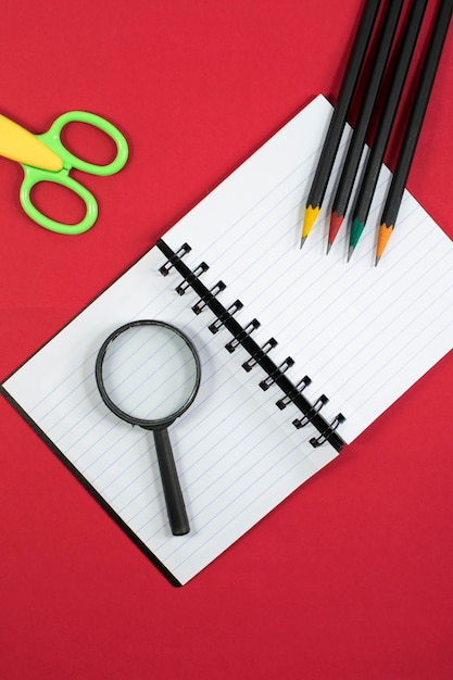 Notebook scissor magnifying glass and colour pencil accessories studying red background