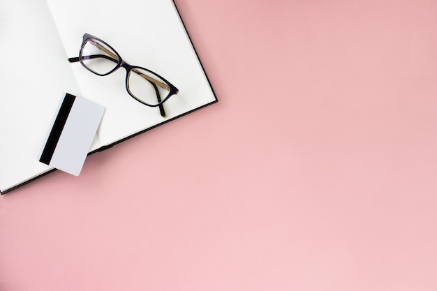 Notebook, sketchbook, eyeglasses, white card on pink background, copy space.