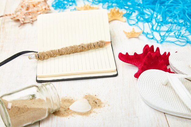 Notebook, starfishes and seashells, glass with sand